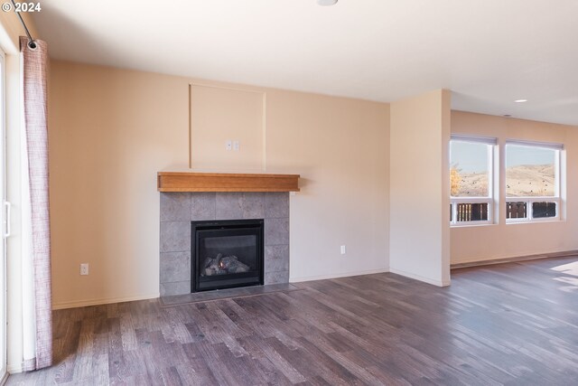 unfurnished living room with a tiled fireplace and dark wood-type flooring