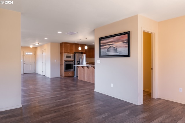 kitchen featuring dark hardwood / wood-style floors, hanging light fixtures, appliances with stainless steel finishes, and a breakfast bar area