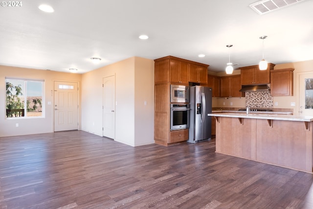 kitchen with dark wood-type flooring, a kitchen breakfast bar, hanging light fixtures, appliances with stainless steel finishes, and tasteful backsplash