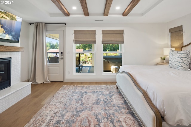 bedroom featuring hardwood / wood-style floors, beam ceiling, and a fireplace