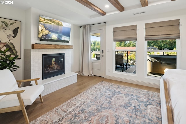 living room featuring light hardwood / wood-style flooring, a brick fireplace, and beam ceiling