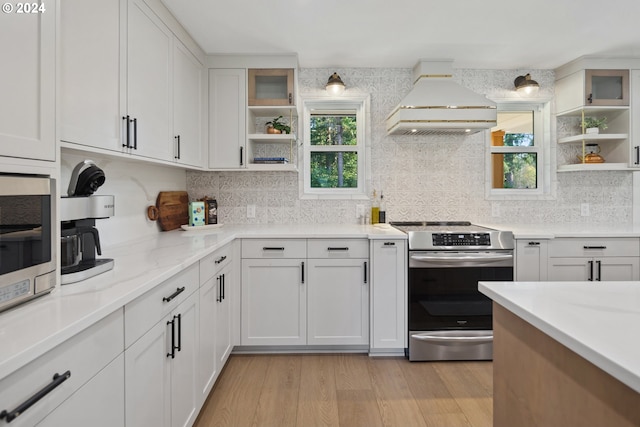 kitchen featuring light stone countertops, appliances with stainless steel finishes, custom exhaust hood, light wood-type flooring, and white cabinets