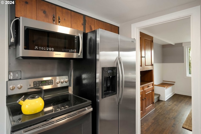 kitchen featuring stainless steel appliances, a wainscoted wall, dark wood-style floors, and brown cabinetry