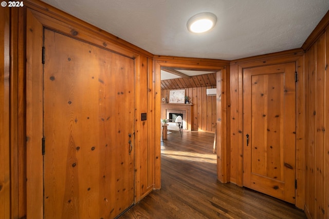 hallway with dark hardwood / wood-style floors, wood walls, and a textured ceiling