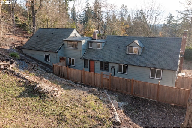 rear view of property with a chimney, roof with shingles, and fence