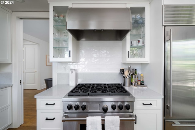 kitchen featuring tasteful backsplash, light stone counters, premium appliances, exhaust hood, and white cabinets