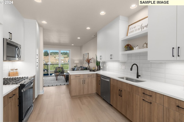 kitchen with kitchen peninsula, appliances with stainless steel finishes, sink, white cabinets, and light hardwood / wood-style floors