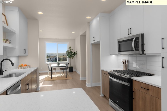 kitchen with appliances with stainless steel finishes, light wood-type flooring, white cabinetry, and sink