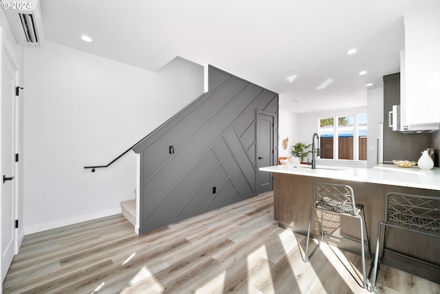 kitchen featuring sink, a wall mounted air conditioner, kitchen peninsula, light hardwood / wood-style floors, and a breakfast bar area