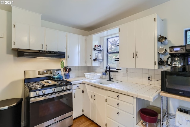 kitchen with white cabinets, sink, backsplash, tile countertops, and gas stove