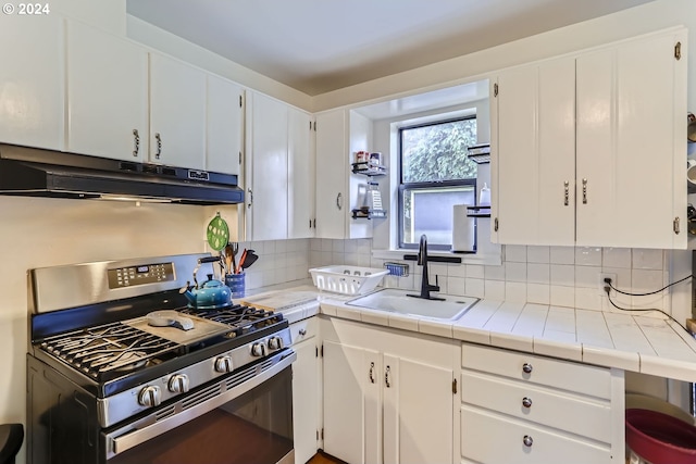 kitchen featuring tile counters, white cabinets, sink, and stainless steel range with gas cooktop