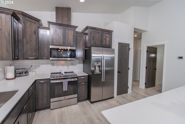 kitchen with tasteful backsplash, light countertops, appliances with stainless steel finishes, vaulted ceiling, and dark brown cabinetry