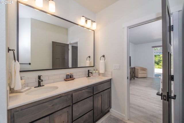 bathroom featuring wood finished floors, a sink, decorative backsplash, and double vanity