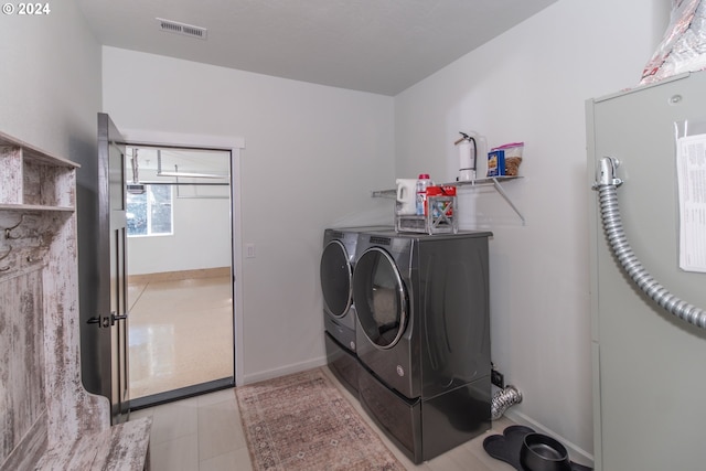 laundry room featuring washing machine and clothes dryer, light tile patterned floors, visible vents, laundry area, and baseboards