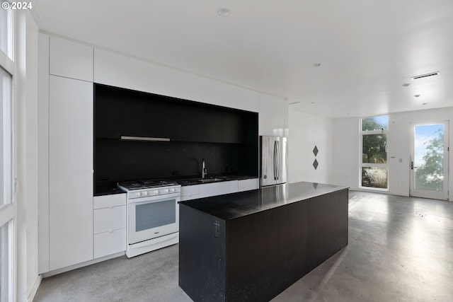 kitchen with gas range gas stove, white cabinetry, stainless steel refrigerator, sink, and a kitchen island