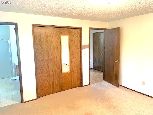 unfurnished bedroom featuring light colored carpet, a textured ceiling, and connected bathroom