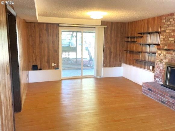 unfurnished living room featuring a brick fireplace, a textured ceiling, and light hardwood / wood-style floors