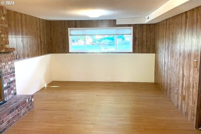 unfurnished living room with a textured ceiling, light hardwood / wood-style flooring, and wood walls