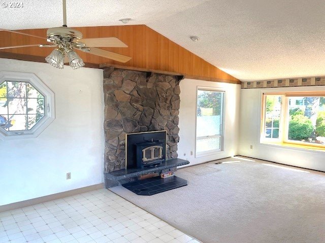 unfurnished living room with ceiling fan, a textured ceiling, lofted ceiling, and a wood stove