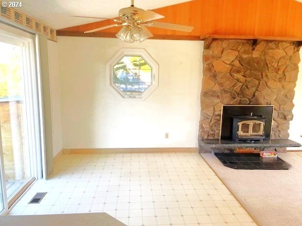 unfurnished living room featuring ceiling fan, vaulted ceiling, a wood stove, and a wealth of natural light