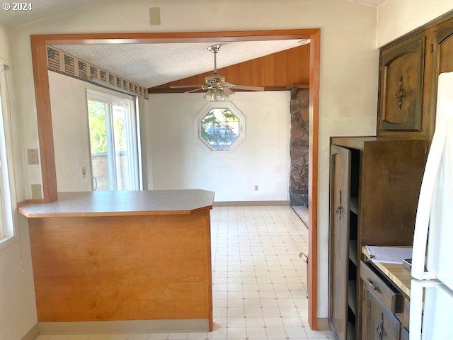 kitchen with ceiling fan, white refrigerator, lofted ceiling, kitchen peninsula, and a textured ceiling