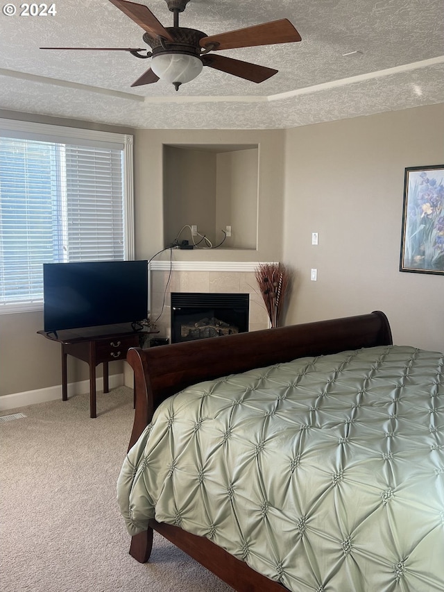 carpeted bedroom featuring ceiling fan, a textured ceiling, and a tile fireplace