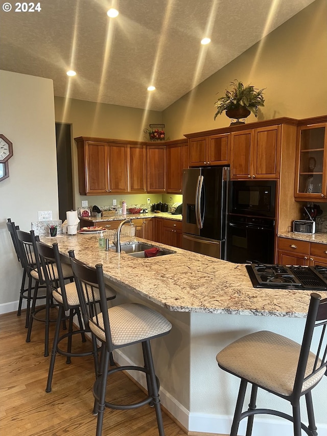 kitchen with black appliances, light hardwood / wood-style floors, lofted ceiling, and a breakfast bar area