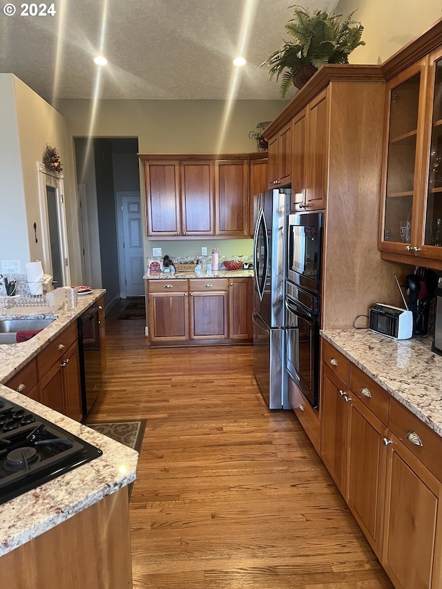 kitchen with light stone counters, sink, black appliances, and light wood-type flooring