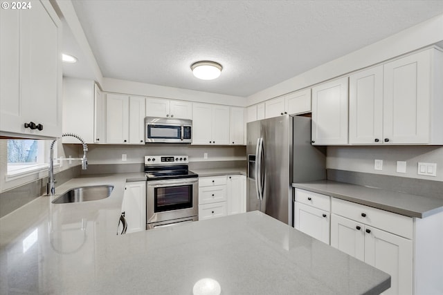 kitchen featuring a textured ceiling, stainless steel appliances, white cabinetry, and sink