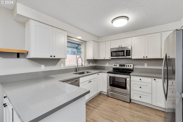 kitchen with a textured ceiling, stainless steel appliances, sink, light hardwood / wood-style flooring, and white cabinets