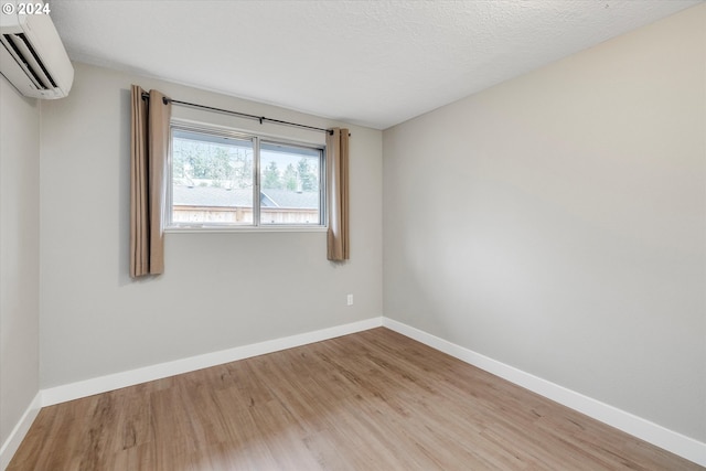 spare room featuring wood-type flooring, a textured ceiling, and an AC wall unit