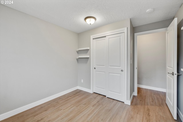 unfurnished bedroom featuring a textured ceiling, light wood-type flooring, and a closet