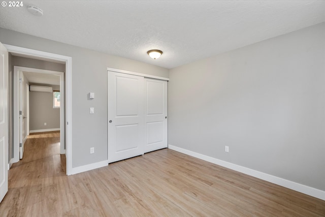 unfurnished bedroom featuring a closet, a textured ceiling, a wall unit AC, and light hardwood / wood-style flooring