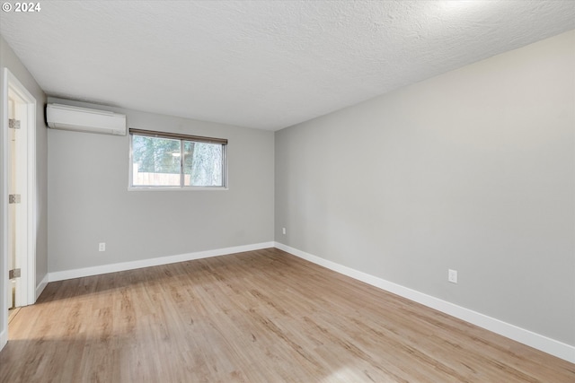 empty room with a wall mounted air conditioner, a textured ceiling, and light hardwood / wood-style flooring