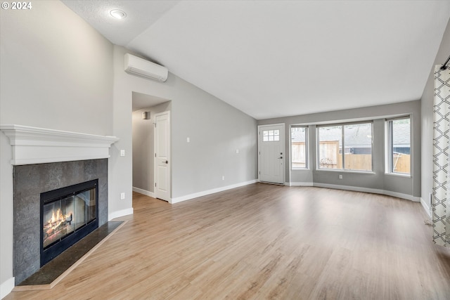 unfurnished living room featuring an AC wall unit, a tiled fireplace, light hardwood / wood-style floors, and vaulted ceiling