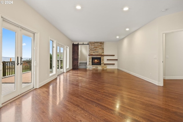 unfurnished living room featuring a stone fireplace, a barn door, wood-type flooring, and a wealth of natural light