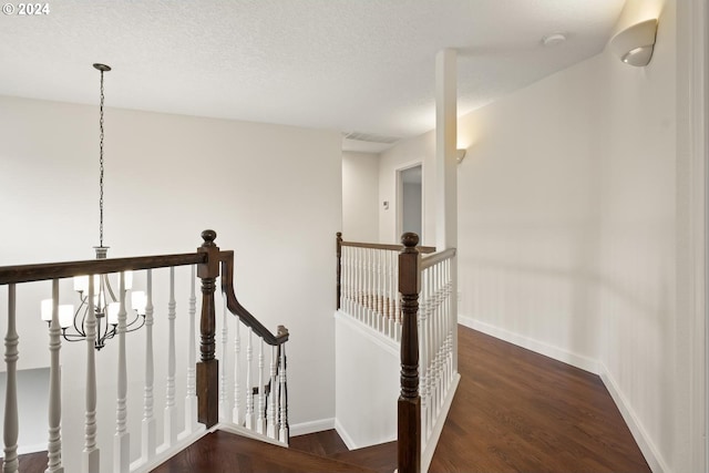 hallway with dark wood-type flooring, a notable chandelier, and a textured ceiling