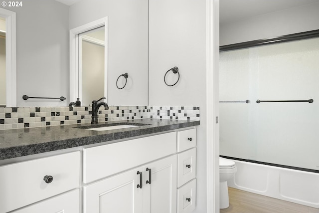 full bathroom featuring wood-type flooring, toilet, bath / shower combo with glass door, vanity, and decorative backsplash