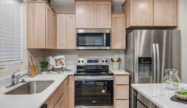 kitchen with appliances with stainless steel finishes, sink, light brown cabinets, and light stone counters