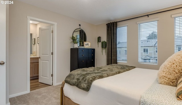 bedroom featuring light carpet, ensuite bathroom, and baseboards