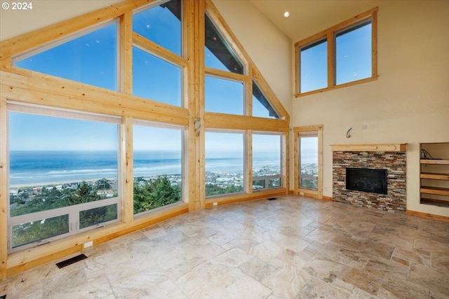 unfurnished living room featuring a stone fireplace, a water view, high vaulted ceiling, and a wealth of natural light