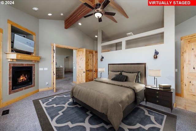 bedroom with lofted ceiling with beams, a tile fireplace, carpet flooring, ceiling fan, and ensuite bath