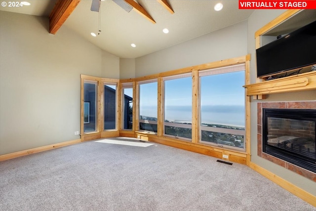 unfurnished living room featuring a tiled fireplace, ceiling fan, beamed ceiling, and carpet flooring