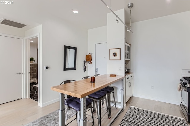 kitchen featuring stainless steel electric range, white cabinetry, decorative light fixtures, and light hardwood / wood-style flooring