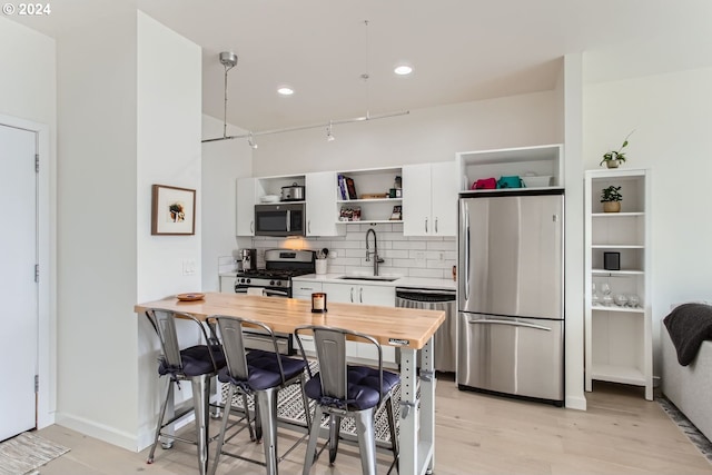 kitchen with appliances with stainless steel finishes, a kitchen breakfast bar, sink, light hardwood / wood-style flooring, and white cabinetry