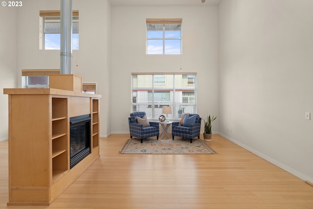 sitting room with light hardwood / wood-style flooring, a towering ceiling, a tile fireplace, and a wealth of natural light