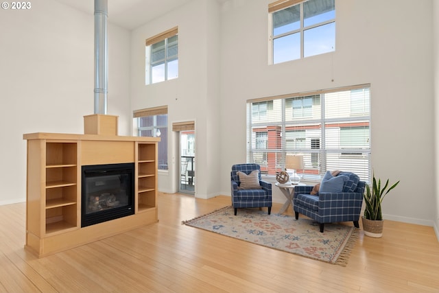 living area with a healthy amount of sunlight, a towering ceiling, and hardwood / wood-style flooring