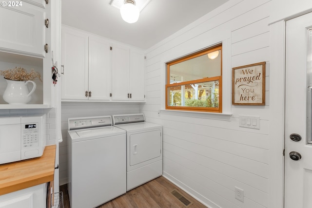 laundry room with washer and dryer, cabinets, wooden walls, and light hardwood / wood-style floors