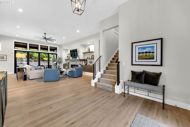 living room with a stone fireplace, ceiling fan with notable chandelier, and light hardwood / wood-style floors