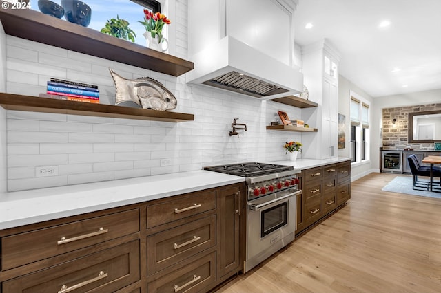 kitchen with wall chimney exhaust hood, backsplash, premium range, light hardwood / wood-style floors, and white cabinets